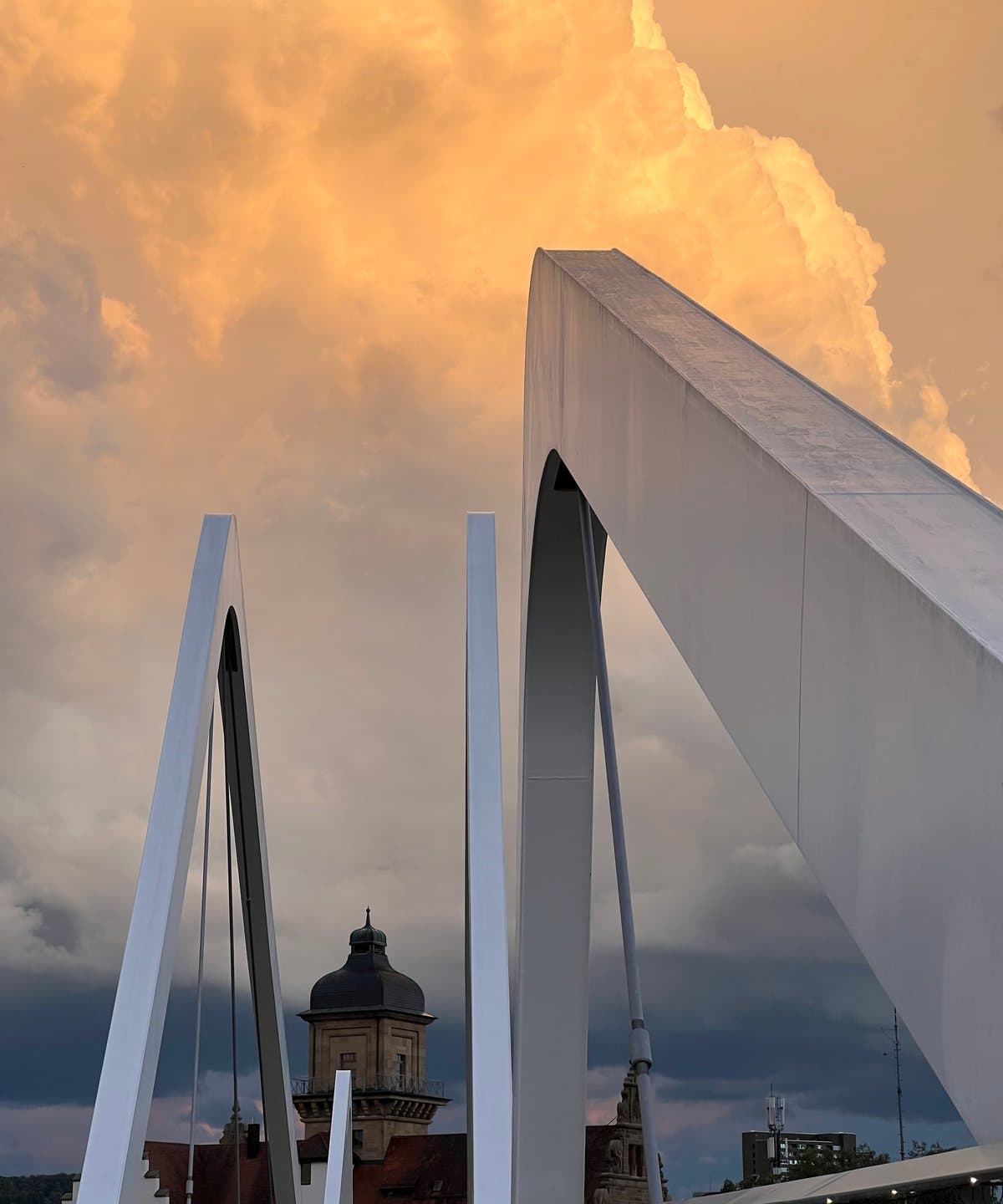 Die weißen Bögen einer Fußgängerbrücke vor einer goldenen Gewitterwolke, Heilbronn, 28. August 2026.
